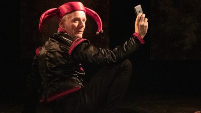 En man föreställande Gustav Vasa står på en teaterscen och tar en selfie med en mobiltelefon