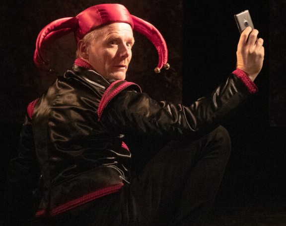 En man föreställande Gustav Vasa står på en teaterscen och tar en selfie med en mobiltelefon