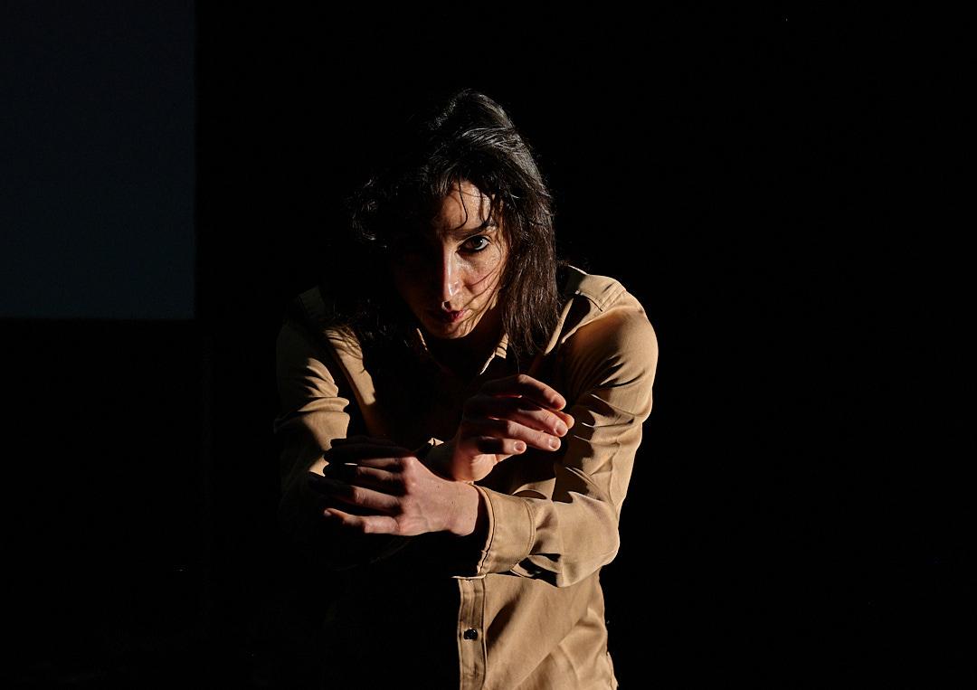 Bild på en dansare med huvtröja, med ansiktet halvt dolt i skugga, ena ögat tittar intensivt i kameran