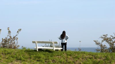 Kvinna står framför en bänk och ser ut över havet.