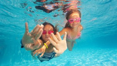 Två glada flickor simmar under vattnet