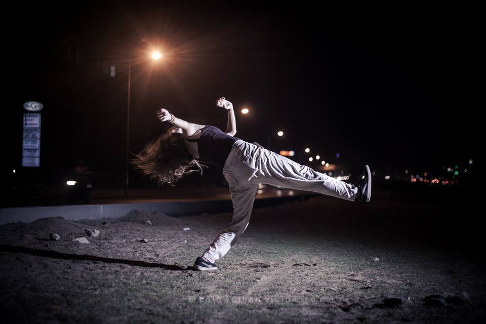 En kvinna som dansar i gatlyktans sken med stadens alla ljus i bakgrunden